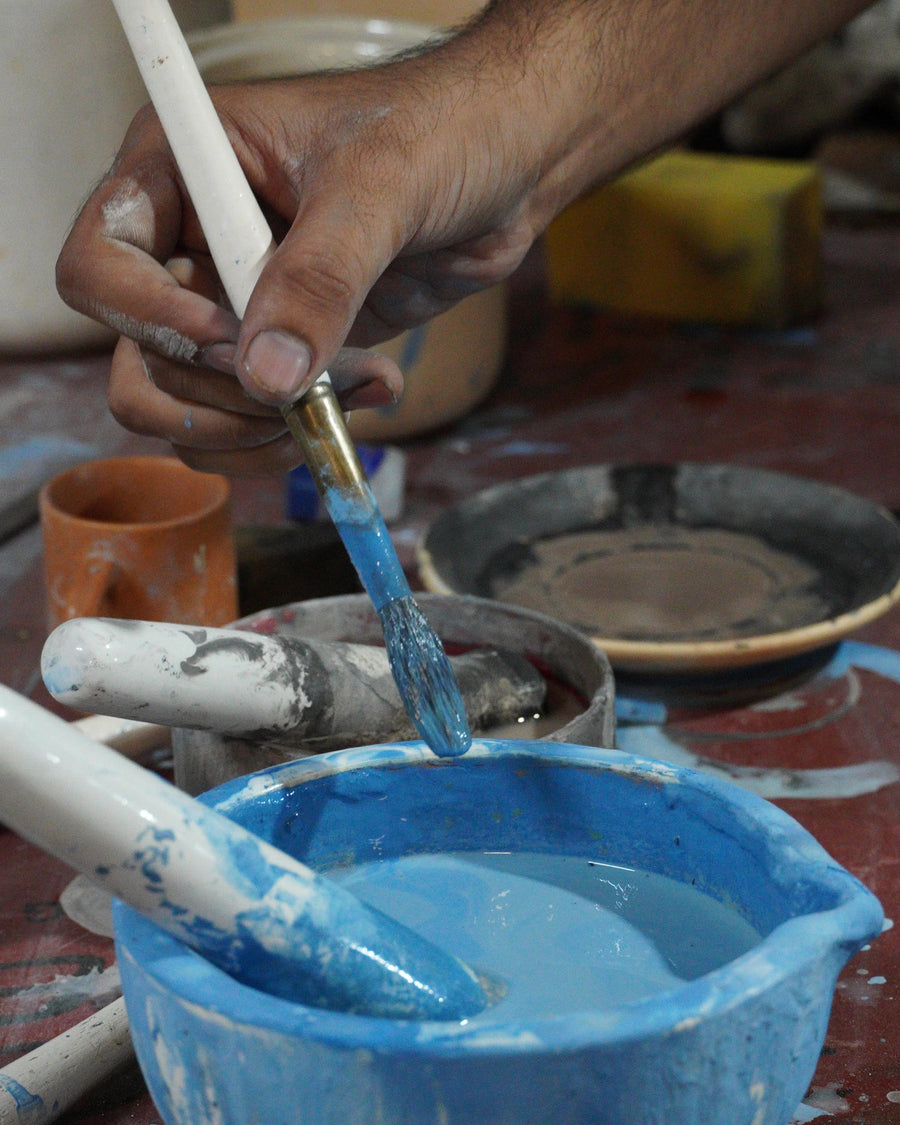Person mixing blue paint in a bowl with a brush on a pottery wheel.