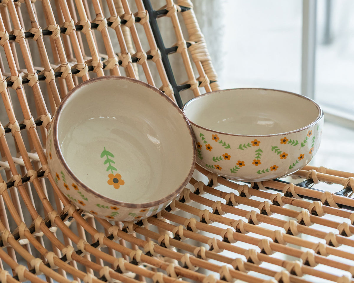 Two ceramic bowls with floral patterns on a woven surface.