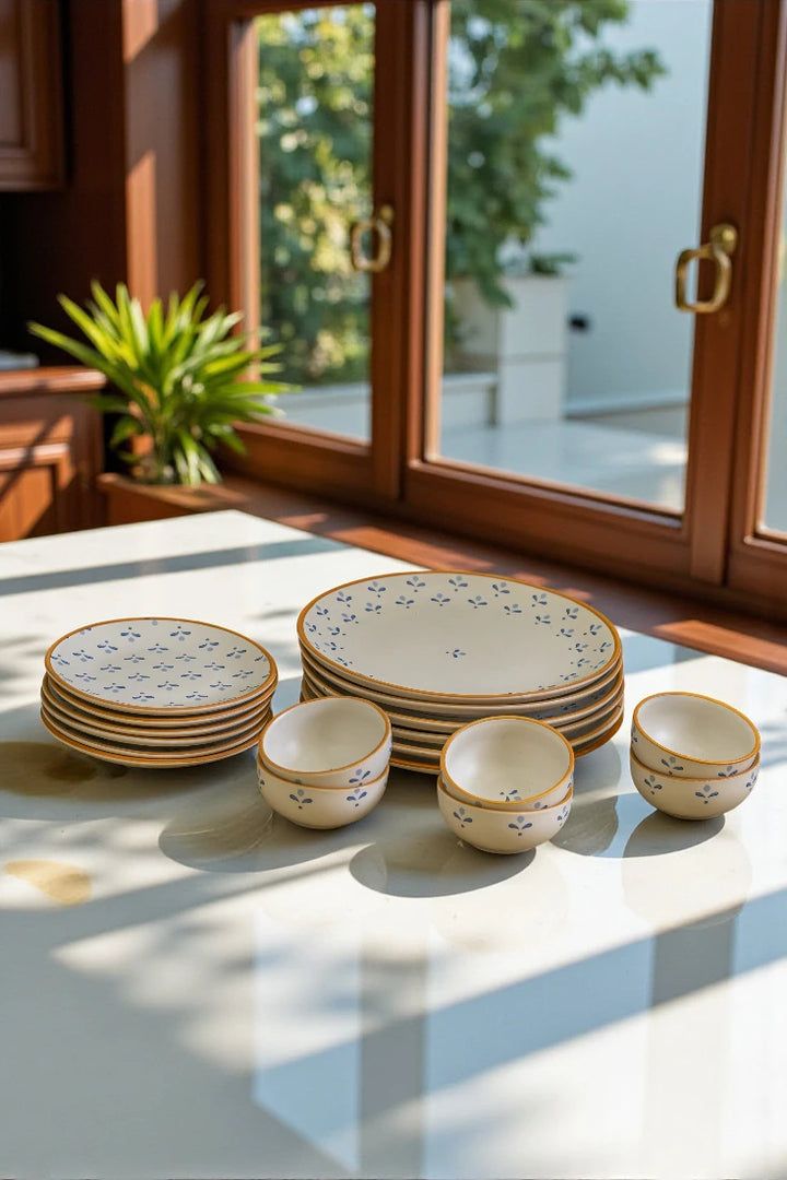 Set of ceramic dishes with floral patterns on a light-colored surface, with a window and outdoor view in the background.