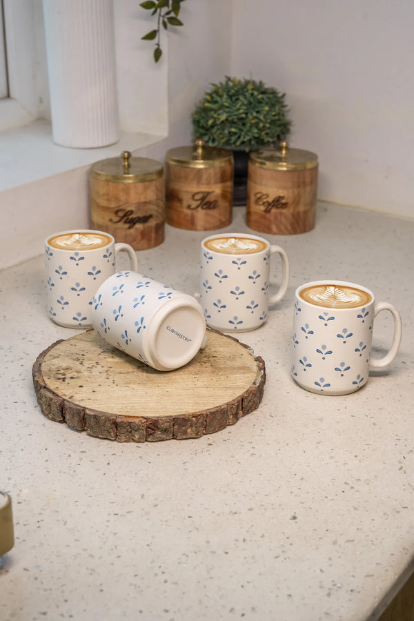 Four mugs with floral patterns on a countertop with wooden canisters in the background.