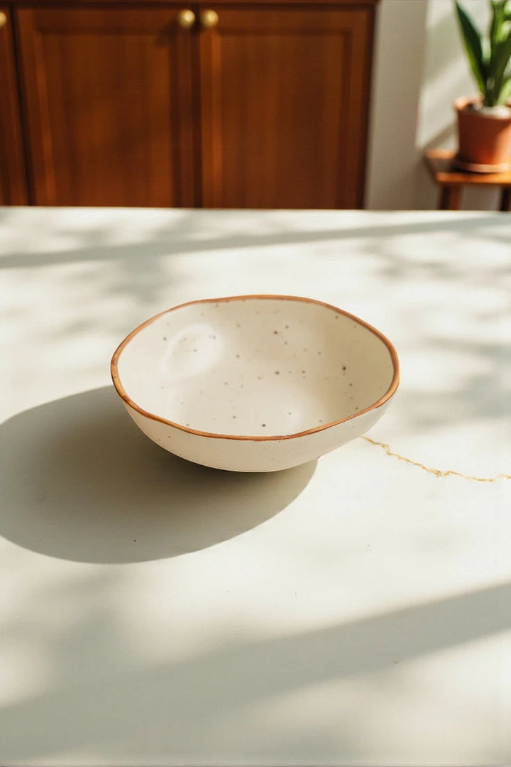White ceramic bowl with brown rim on a light surface with wooden cabinets in the background