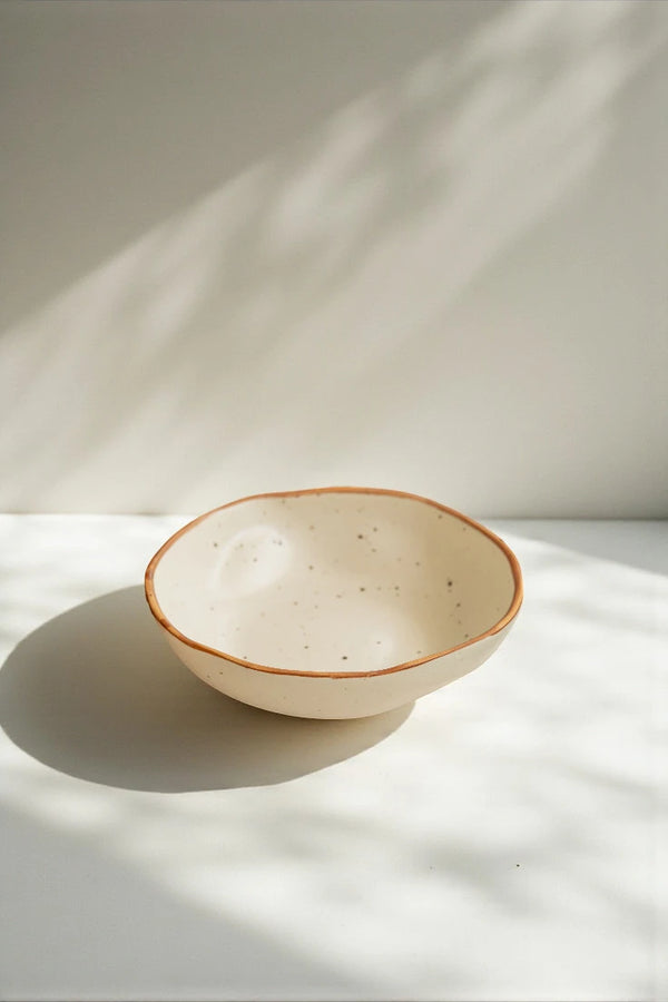 Ceramic bowl with brown rim on a white surface with soft shadows