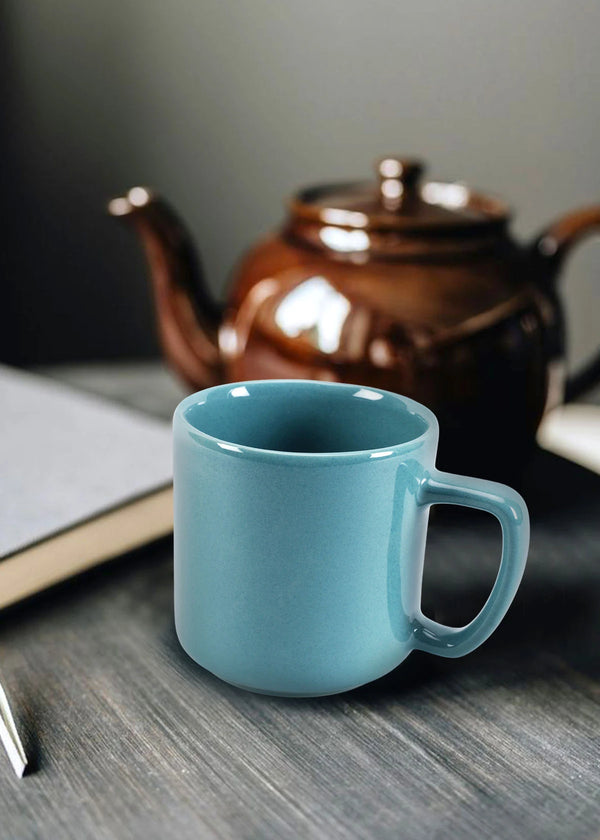 Teal mug on a wooden surface with a brown teapot in the background