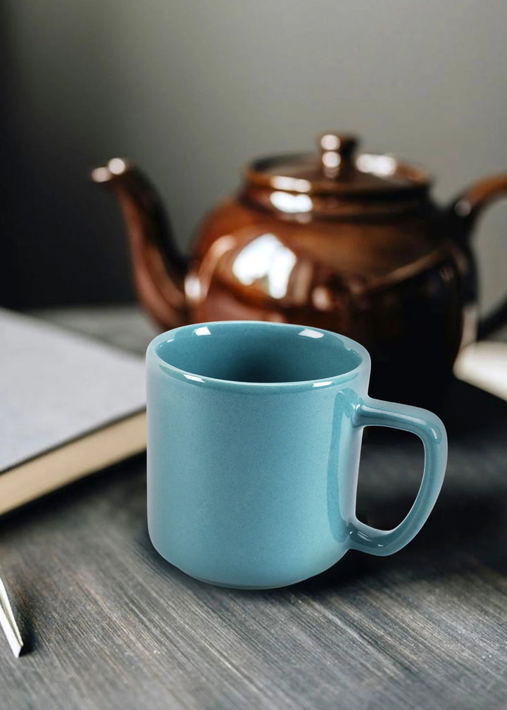 Teal mug on a wooden surface with a brown teapot in the background
