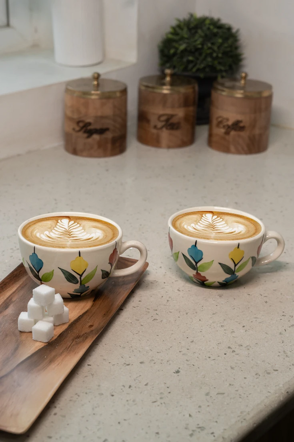 Two floral-patterned coffee cups with latte art on a kitchen counter.