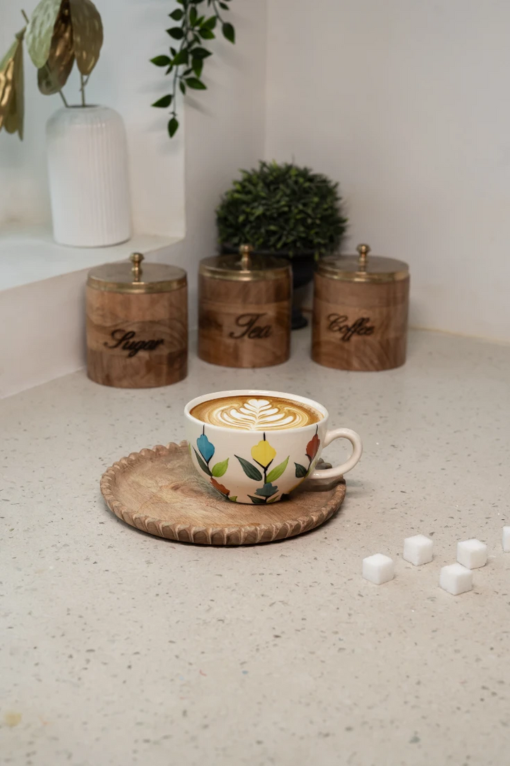 Cup of coffee with decorative foam on a textured surface, surrounded by wooden containers labeled 'Tea' and 'Coffee'.