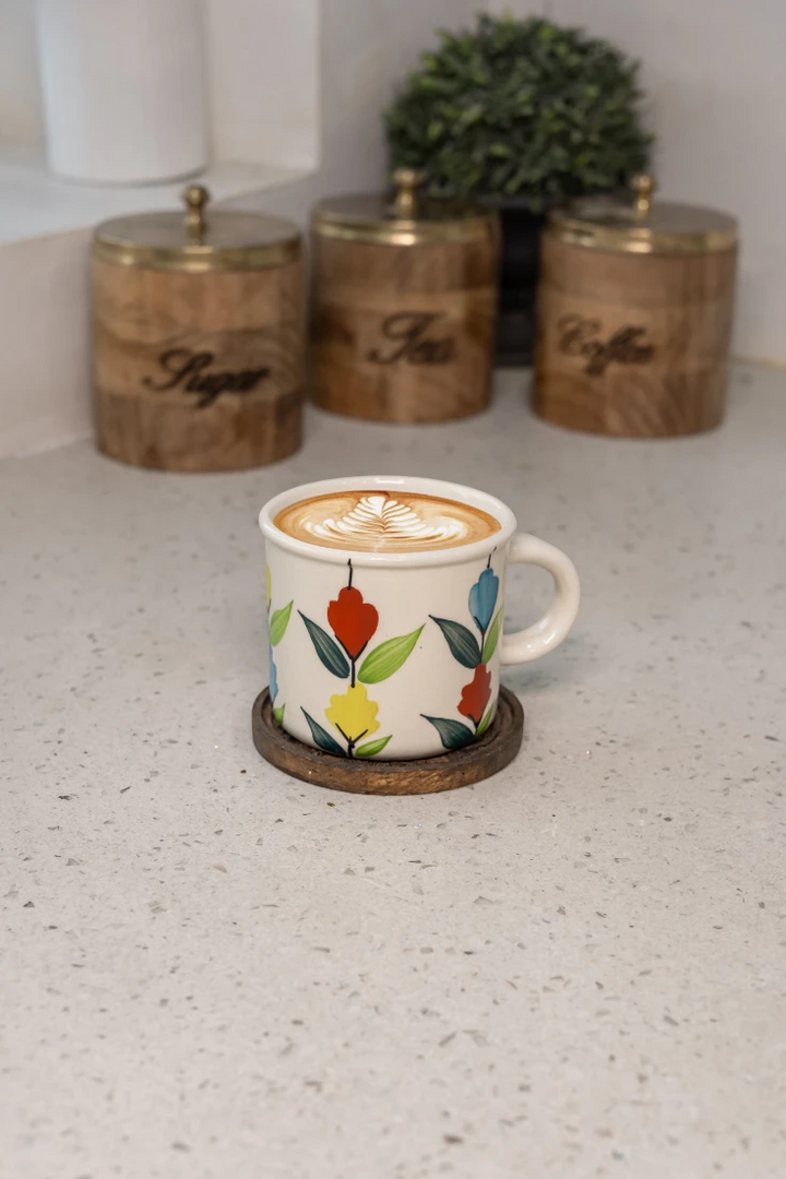 Cup of coffee with a colorful design on a white countertop with wooden canisters in the background.