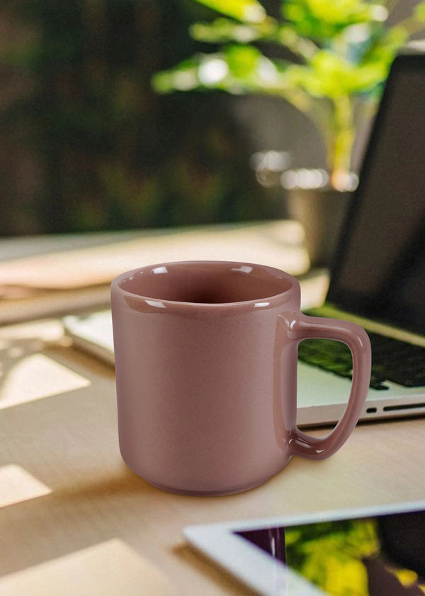 Pink mug on a desk with a laptop and plant in the background