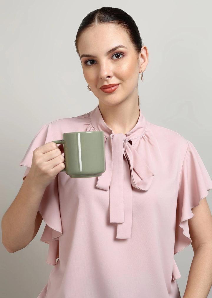 Woman in a pink blouse holding a green mug against a plain background