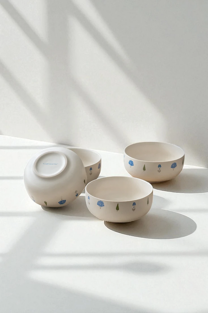 Four The Solitude ceramic decorative bowls arranged on a white surface with dramatic shadows, one inverted to show the base. The blue tree patterns are visible on these high-quality kitchen crockery pieces.