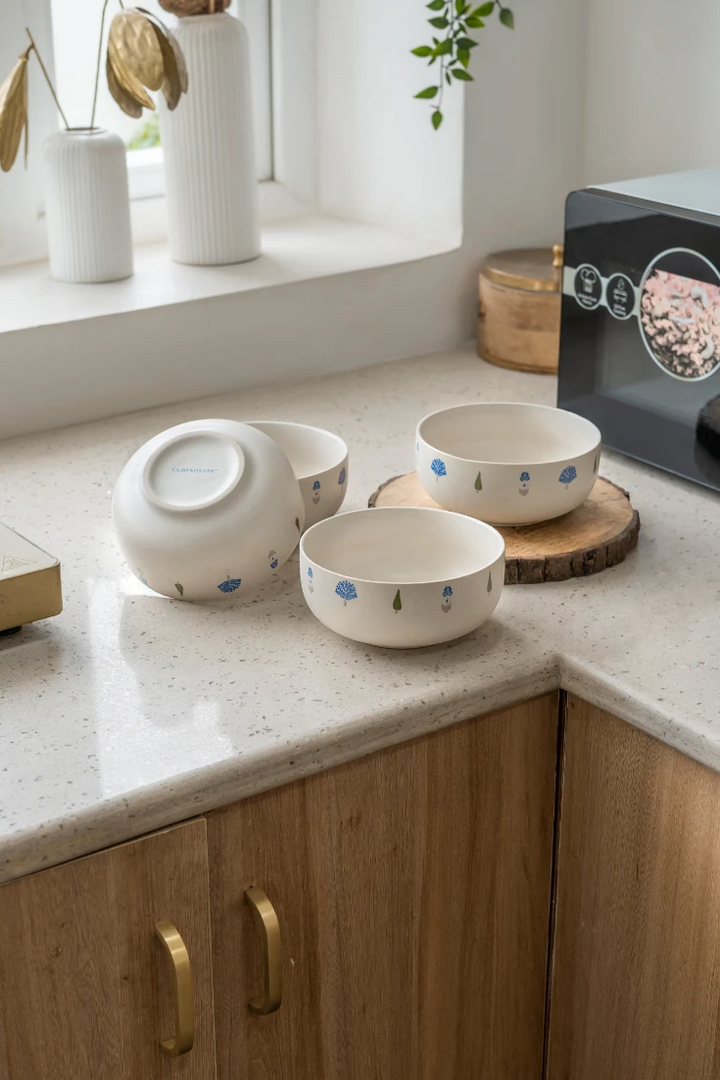 A collection of The Solitude high-quality kitchen crockery bowls arranged on a modern kitchen counter. One bowl is inverted, revealing the 'Claymistry' brand on its base. These are microwave safe ceramic bowls that blend functionality with beautiful design.