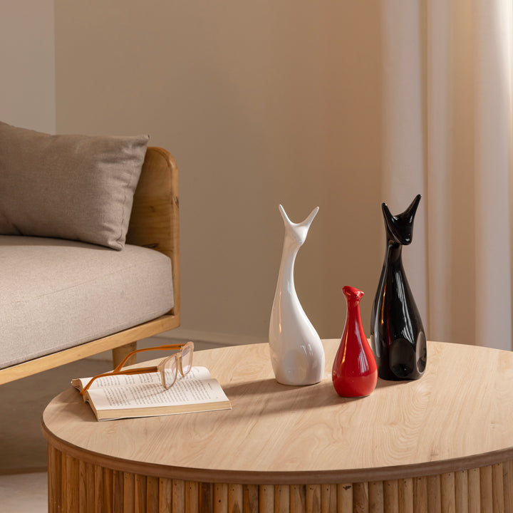 3 ceramic deer-shaped figurines on a wooden table beside glasses and an open book, with a sofa in the background