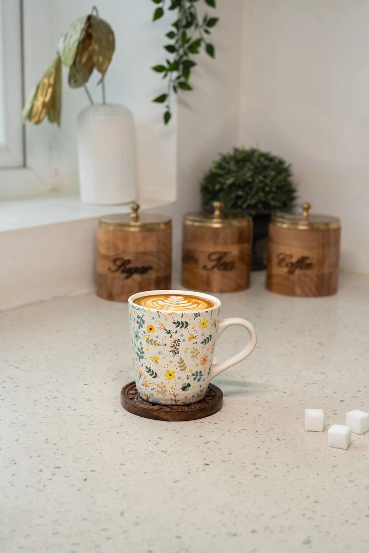 Decorative mug with floral pattern on a white countertop with wooden canisters in the background.