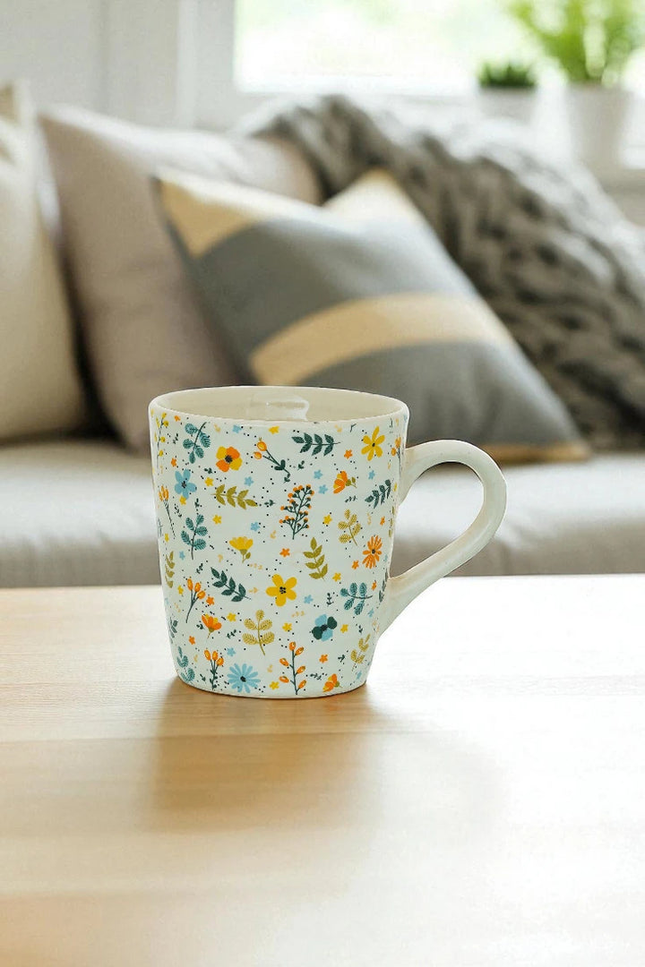 Floral-patterned mug on a wooden surface with a blurred background of a living room.