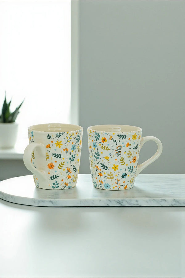 Two floral-patterned mugs on a marble surface with a neutral background