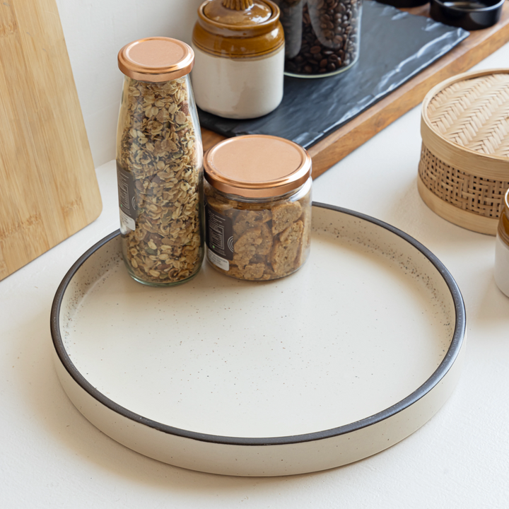 Handmade round ceramic tray in sand with black rim, non-toxic and perfect for stylish serving & decor.