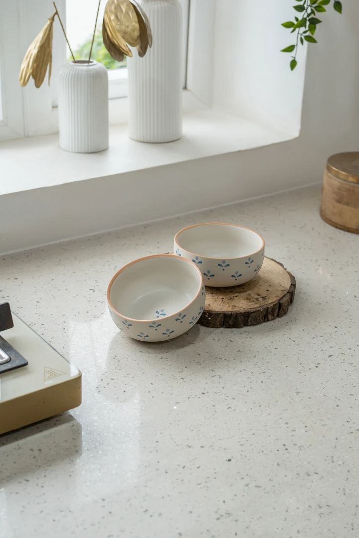 Two ceramic bowls on a wooden coaster on a speckled countertop with decorative elements.